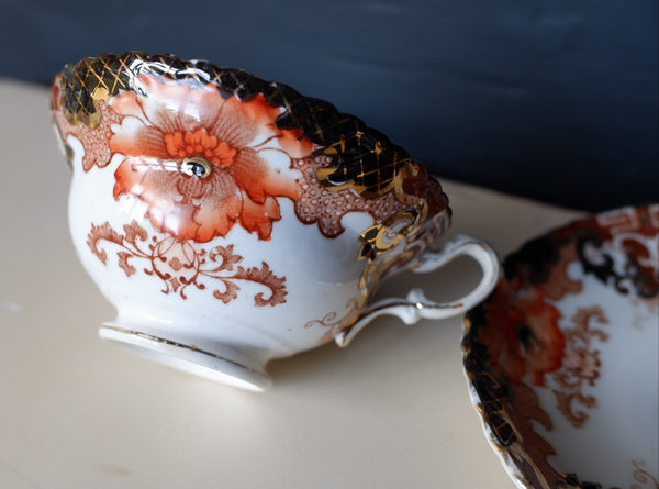 A white porcelain teacup with a large orange floral design, gold detail