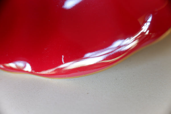 A close-up of a glossy red ceramic plate or bowl edge with a scalloped rim, resting on a light beige textured surface.