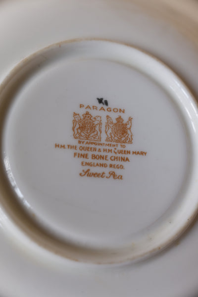 The underside of a vintage white porcelain tea cup or saucer, featuring gold printed text and crest logos. The text reads 'PARAGON' and 'by appointment to HM THE QUEEN & HM QUEEN MARY FINE BONE CHINA ENGLAND REGD.