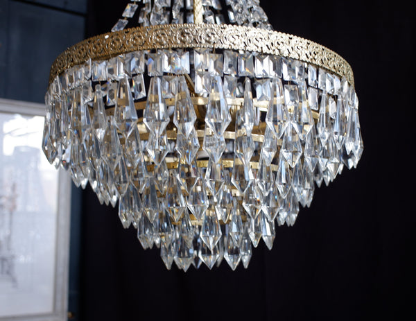 A close-up of a crystal chandelier with clear faceted hanging prisms and a gold-toned metal frame, shown against a dark background.