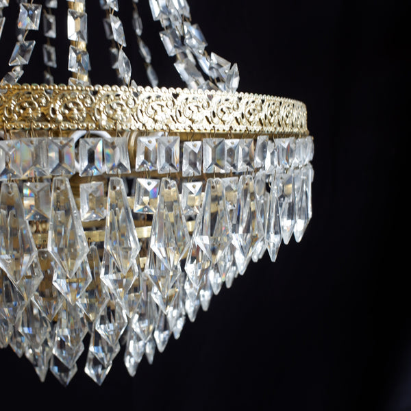 Close-up of a crystal chandelier with clear faceted hanging drops and a gold-toned metal band against a black background.