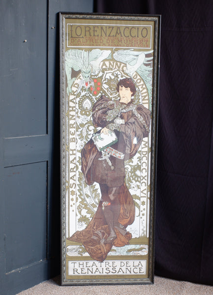 A framed vintage Art Nouveau poster leaning against a dark blue door and black curtain backdrop. The poster features an illustrated woman in flowing brown and beige robes with decorative text including 'LORENZACCI0' at the top and 'THEATRE DE LA RENAISSANCE' at the bottom.