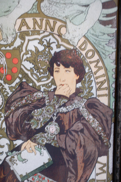 A close-up of an Art Nouveau style illustration featuring a woman in ornate brown and silver clothing, with decorative text reading 'ANNO DOMINI' and a crest in the background.