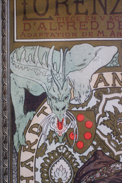 Close-up of an illustrated book cover or printed artwork featuring a pale green dragon above ornate decorative lettering and a shield with red dots.