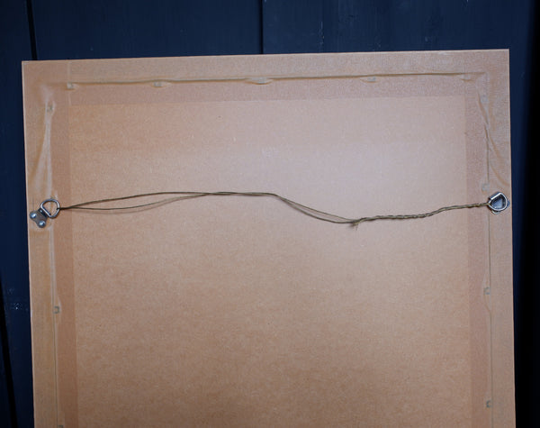 The back of a square picture frame or canvas, showing a tan cardboard backing, mounting hardware, and hanging string against a dark blue background.