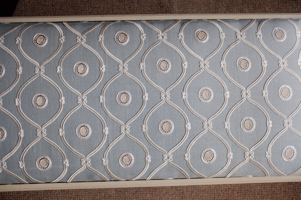 A close-up of a textured fabric panel featuring a repeating geometric trellis pattern in light blue with cream and beige accents.